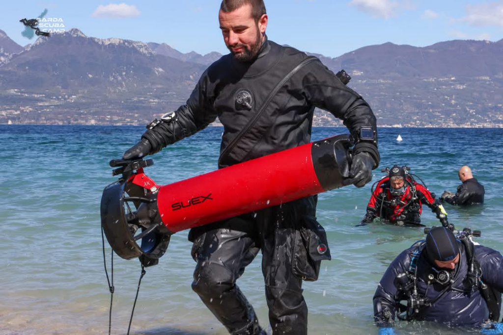 Uomo esce dal Lago di Garda con uno scooter subacqueo SUEX rosso durante il Garda Scuba Camp 2025.